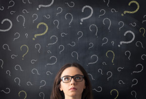 Chalk question marks above businesswoman at blackboard